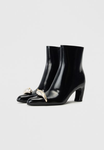 Black leather ankle boots with a glossy finish, pointed toe design, and notable metallic accents at the front and heel.
