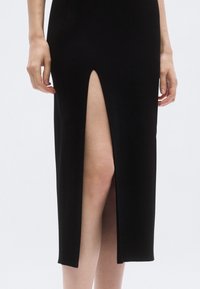 Čierne rebrované midi šaty s rozparkom nad stehno, priliehavým strihom a jemnou textúrou, s rovnomerným lemom na spodku.