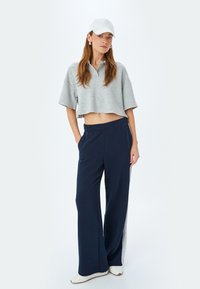Grå kortærmet polo skjorte, parret med marineblå brede bukser med sidelange striber. Hvid kasket og sko fuldender outfittet.