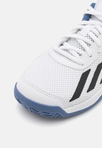 Witte sportschoen met een bovenwerk van mesh, zwarte accenten en een blauwe zool. Heeft een gestructureerde stof, een traditioneel vetersysteem en een lichte curve in het ontwerp.