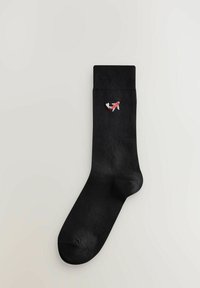 Fekete zokni bordás szegéllyel, az oldalán egy kicsi piros és fehér hímzett koi hal mintával. Simaságával tűnő anyagtextúra.