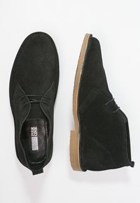 Bottines en daim noir avec un bout rond, un détail en dentelle, une semelle en caoutchouc et une semelle intérieure texturée. Fini lisse avec des accents minimaux.