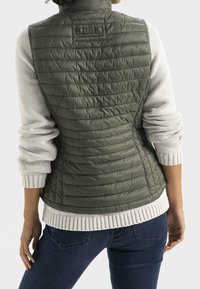 Olijfgroene gewatteerde vest met een hoge kraag, doorgestikte ontwerpen, en een lichtgrijze gebreide trui eronder, met ribgebreide manchetten en zoom.