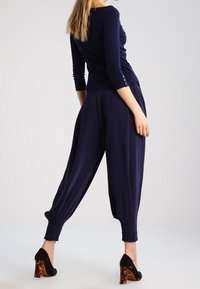 Námořnické modré přiléhavé tričko s tříčtvrtečními rukávy v kombinaci s volnými tmavými kalhotami s zúženým kotníkem. Černé podpatky s želvovinovými akcenty.