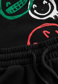 Sort sweatshirtstof med farverige smiley-face grafikker i grøn, hvid og rød. Elastisk talje med justerbar snøre.