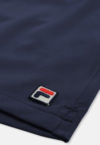 Tissu bleu marine avec ourlet cousu et petite écusson rectangulaire rouge, blanc et bleu marine près du bord.