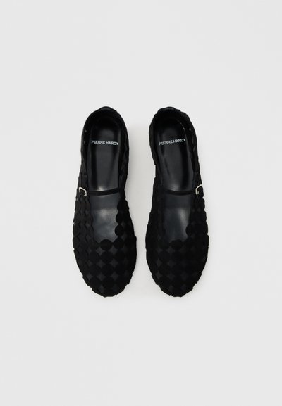 Black slip-on shoes with a textured surface featuring diamond patterns, leather accents, and a silver buckle detail on the upper section.
