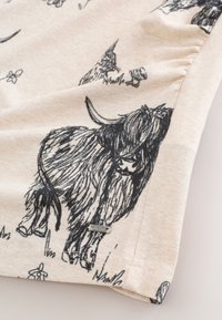 Tissu crème avec dessins au trait noirs d'une vache des Highlands, d'oiseaux, d'herbe et de fleurs, avec une petite étiquette métallique de marque.