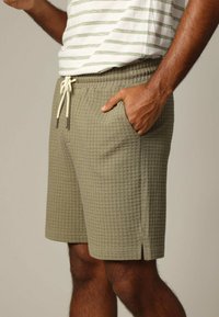 Khaki shorts met een gestructureerd, wafelgebreid ontwerp, een trekkoord in de taille en zijzakken. De shorts eindigen boven de knie met kleine zijsplitsingen.
