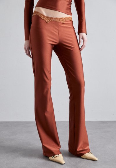 Pantalons couleur rouille avec une texture satinée lisse, présentant une bordure en dentelle festonnée à la taille. Design à jambes évasées.