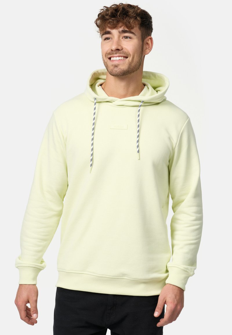 Lichtgele hoodie met een trekkoordcapuchon, ribgebreide manchetten en zoom. Beschikt over een klein label aan de voorkant en een zachte textuur. Zwarte broek.