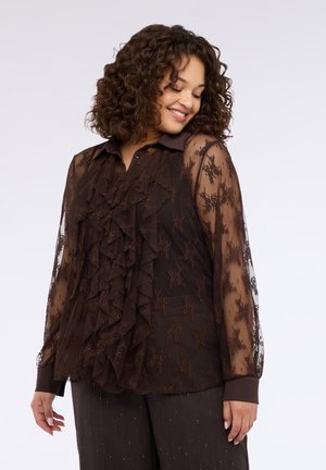 Blusa trasparente marrone scuro con volant sovrapposti, motivo floreale e maniche lunghe. Presenta un colletto appuntito e dettagli con bottoni sui polsini.