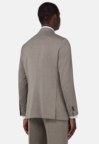 Chaqueta de traje gris claro con una tela texturizada, abertura simple en la parte posterior y acentos de puños abotonados. Presenta un corte ajustado y solapas lisas.