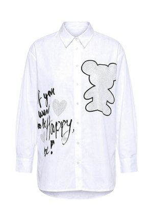 Camisa blanca abotonada con un gran gráfico de un oso de peluche delineado y texto manuscrito en negro que dice "Si quieres ser feliz, sé" con corazones.