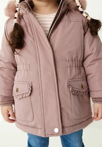 Roze geïsoleerde jas met gerimpelde zakken, gouden knoopaccenten en een nep-bont pompon op de capuchon, gecombineerd met een gestreept shirt eronder.