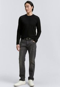 Cămașă neagră cu mâneci lungi, blugi gri, adidași albi. Croială slim fit cu textură netedă și design minimalist, având o curea simplă.