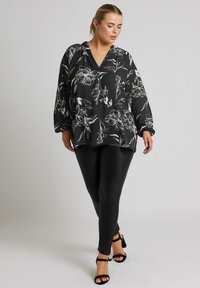 Blusa nera a fiori con motivi floreali bianchi, design a V, maniche larghe abbinata a leggings neri e décolleté neri con cinturini.