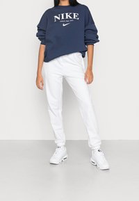 Mörkblå sweatshirt med vit "NIKE" logga, tillsammans med vita joggers och vita sneakers. Sweatshirten har en avslappnad passform och ribbade muddar.