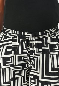 Mønstrede bukser i sort og hvit med et geometrisk design, med elastisk liv og legg for ekstra form og tekstur.