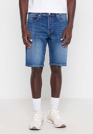 Jeanshorts i mellomvasket blå, med et klassisk fem-lomme-design og rett snitt, brukt med hvite sokker og klumpete sneakers.