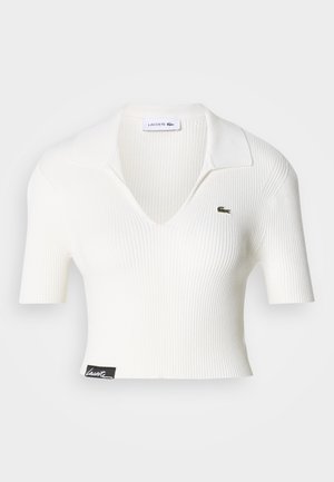 Maglietta polo bianca a coste, corta, con scollo a V, maniche corte e logo coccodrillo verde Lacoste sul petto sinistro. Etichetta nera sull'orlo.