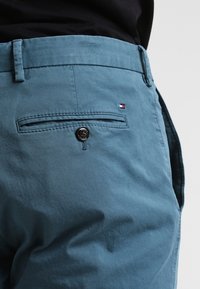 Pantaloni di cotone azzurri chiari con una tasca posteriore con un bottone nero, cuciture sottili e un piccolo logo vicino alla vita.