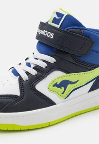 Hochformat Sneaker aus marineblauem und weißem Leder, mit einem leuchtend grünen Akzent und Logo. Verfügt über einen Klettverschluss und weiße Schnürsenkel. Strukturierte Sohle.