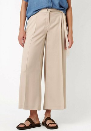 Beige wide-leg cropped pants with a fabric belt worn with brown slide sandals and a blue top.