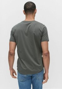 Oliwkowa, krótkozasięgowa koszulka z okrągłym dekoltem, widoczna z tyłu, wykonana z miękkiego materiału. Połączona z niebieskimi dżinsami.