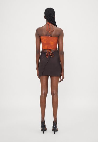 Top orange sans bretelles avec une texture froncée, associé à une mini-jupe noire avec un design en diagonale. Chaussures à talons hauts noires.