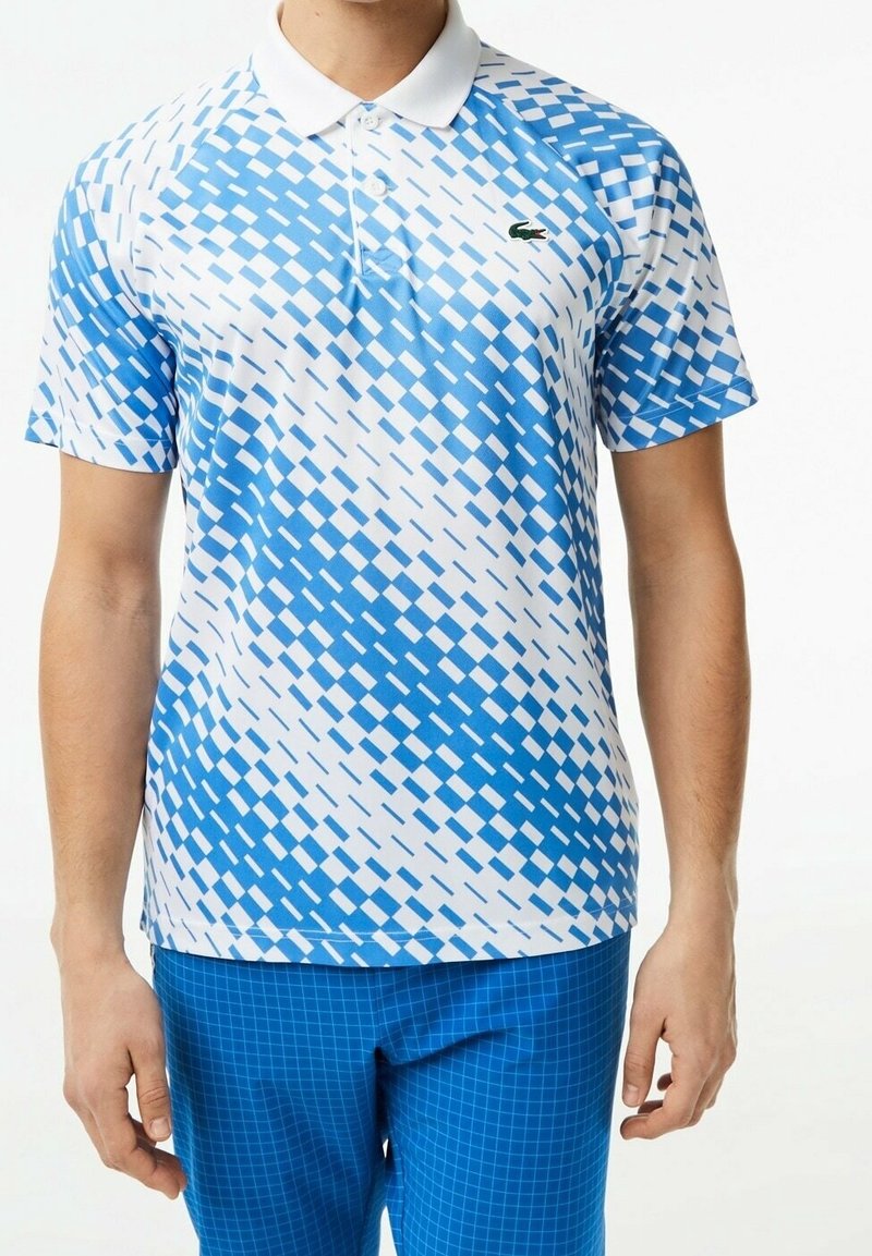 Homme portant un polo à manches courtes avec un motif à carreaux bleu et blanc et un pantalon à carreaux bleu.