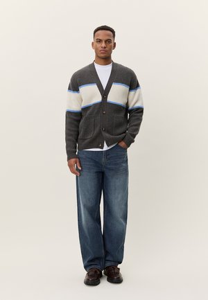 Gray knitted cardigan with white and blue stripes, buttoned front, pocket details. Worn over a white t-shirt and paired with blue jeans.