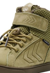 Zapatilla alta de ante verde con un upper de punto texturizado, que presenta un collar acolchado, cordones planos y una correa de Velcro con dos patrones de flechas.