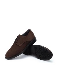 Zapatos de ante marrón con cordones y un acabado suave, con punta redondeada y suela de goma con patrón que presenta gripos circulares para mayor tracción.