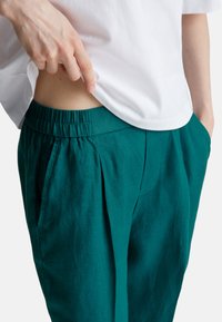 Wrzosowe lniane spodnie z elastycznym paskiem w talii, z przodu z fałdami i kieszeniami bocznymi. Noszone z białym bawełnianym t-shirtem.