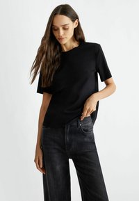 T-shirt nera a maniche corte realizzata in materiale morbido, con una vestibilità rilassata. Abbinata a jeans larghi grigi scuri, che mostrano uno stile casual.