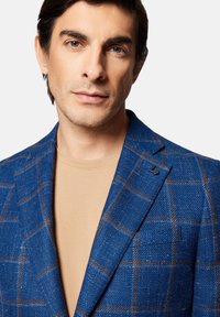 Niebieska marynarka w wzór houndstooth z teksturowanej wełny, z brązowym wzorem w kratę, szpiczastymi klapami oraz subtelnym akcentem logo na kołnierzu.