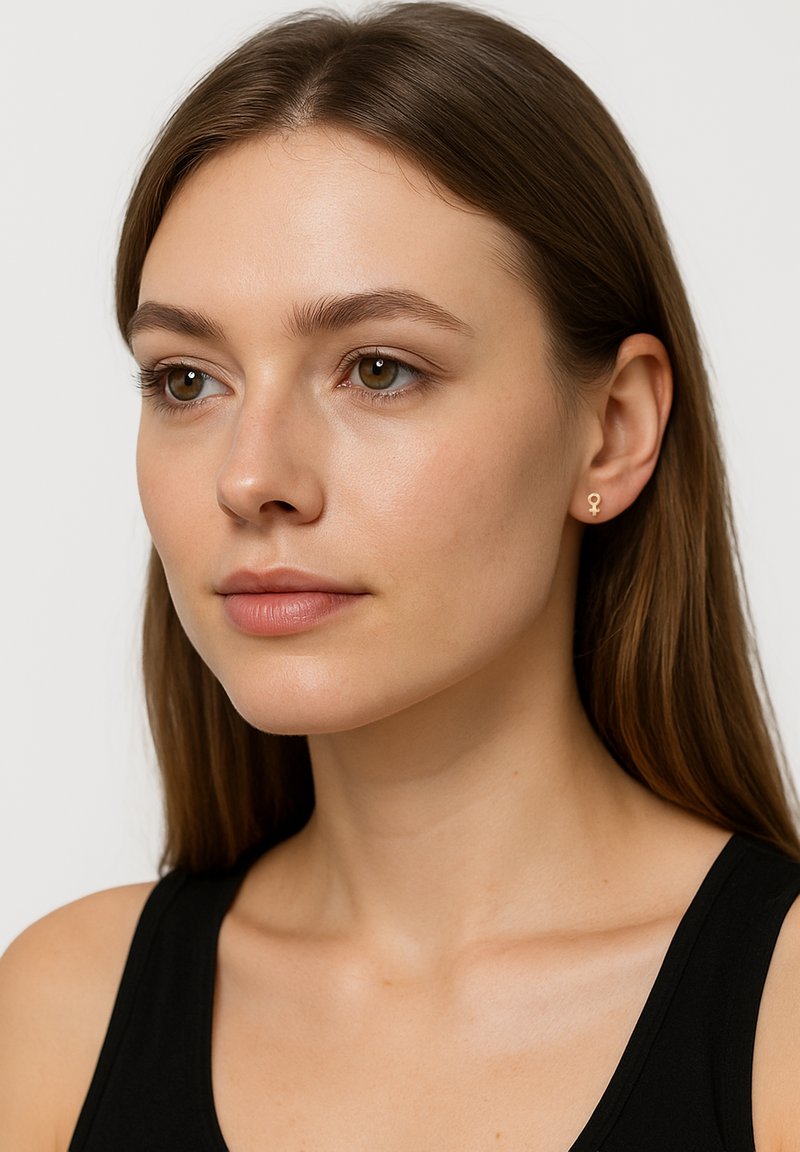 Orecchini a perno in oro a forma di simbolo di genere femminile, piccoli e minimalisti, indossati da un modello con capelli castani lisci e trucco neutro.