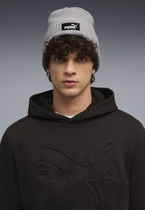 Gray ribbed knit beanie with a black Puma logo patch, worn with a black hooded sweatshirt featuring an embossed Puma design.