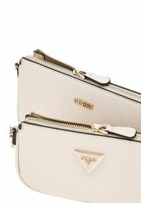 Weißes, strukturiertes synthetisches Handtasche mit goldfarbenen Beschlägen, die mehrere mit Reißverschluss verschlossene Fächer und ein dreieckiges Logo-Accessoire aufweist.