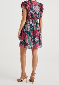 Květinové šaty v zelené, růžové a bílé barvě, s nařaseným pasem, volánkovými rukávy a rozšířenou sukní. Pár nahých sandálů na vysokém podpatku.