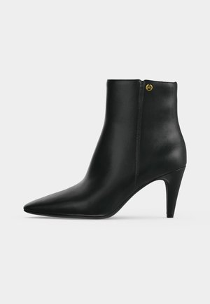 Stivaletto in pelle nera con punta affilata, tacco alto e sottile e piccolo dettaglio logo dorato vicino alla parte superiore sul lato esterno.