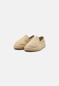 Beige canvas slip-on sko med rund tå, elastiske sidelogoer og vævet jute mellemsål detaljer. Glat tekstur uden synlig branding.