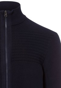 Marineblaue Strickjacke mit Reißverschluss und hohem Kragen, ausgestattet mit strukturiertem Rippmuster über der Brust und einem glatten Reißverschluss vorne.