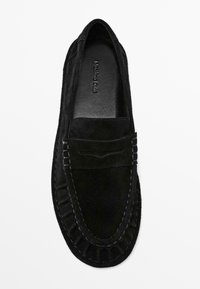 Black suede loafer with a textured finish, featuring a raised seam around the edge and a decorative front panel with stitching details.