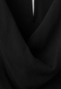 Gros plan d'un tissu noir texturé avec un pli en forme de V et une boutonnière visible en haut au centre.