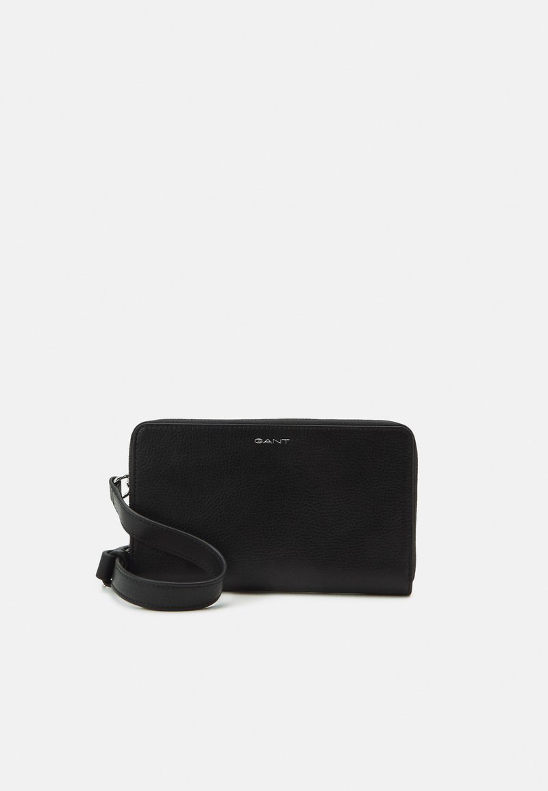 Cartera de muñeca de cuero negro con cierre de cremallera y correa desmontable, nombre de la marca estampado en la parte frontal, colocada plana sobre un fondo blanco.