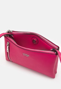 Vaaleanpunainen nahkainen olkalaukku, jossa on teksturoitu pinta, hopeasävyiset vetoketjut ja logo sivussa. Avoin yläosa paljastaa tilavan sisätilan.