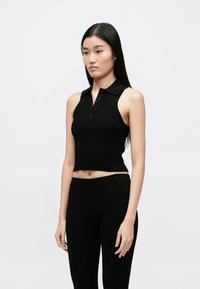 Čierny rebrovaný tielkový polokošeľový top s golierom a zapínaním na gombíky; skrátený strih dopĺňa zladené čierne priliehavé nohavice.