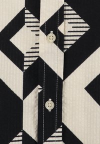 Hemd mit Knöpfen in einem schwarz-weißen geometrischen Muster mit Streifen und Rauten; aus strukturiertem Stoff mit sichtbaren Nähten gefertigt.